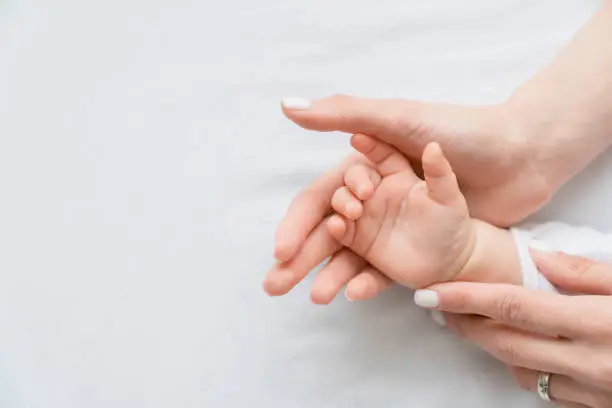 Photo of Close up image of a mother`s mom hand holding her little small toddler`s infant newborn tiny hand on white background. Childcare, motherhood concept.
