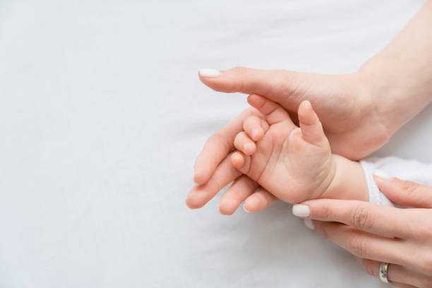 close up image of a mother`s mom hand holding her little small toddler`s infant newborn tiny hand on white background. childcare, motherhood concept. - human fertility imagens e fotografias de stock