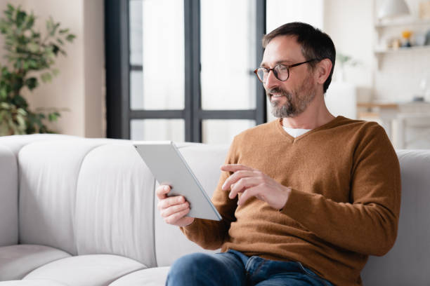 istock Relaxed mature middle-aged man using tablet, typing messages in social media, reading e-book, e-learning online on quarantine at home. 1328351373