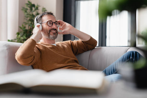 Chilling relaxed mature man father husband listening to the music in headphones lying on the sofa, enjoying sound tracks remotely. Break from working from home. Chilling relaxed mature man father husband listening to the music in headphones lying on the sofa, enjoying sound tracks remotely. Break from working from home. audio book stock pictures, royalty-free photos & images