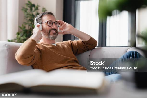 Chilling Relaxed Mature Man Father Husband Listening To The Music In Headphones Lying On The Sofa Enjoying Sound Tracks Remotely Break From Working From Home Stock Photo - Download Image Now