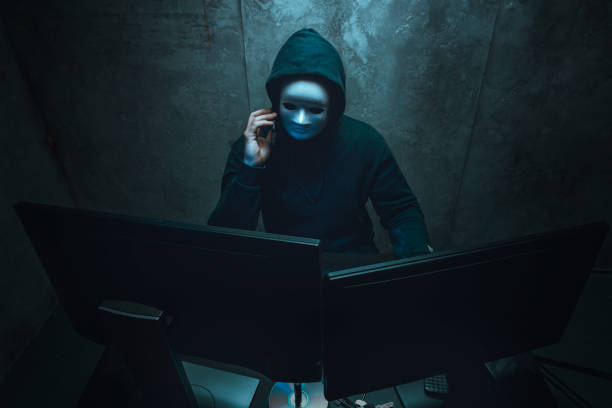 hacker anonimo che indossa la maschera facciale che lavora al computer nella stanza buia - anonymous rete di attivisti foto e immagini stock