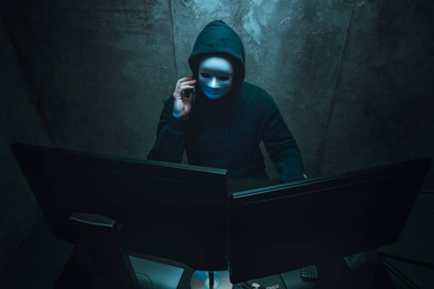 Anonymous hacker wearing face mask working on computer in dark room Anonymous hacker wearing face mask working on computer in dark room, close up anonymous activist network stock pictures, royalty-free photos & images