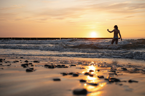 silhouette of little girl standing in the waves of baltic sea at sunset hour