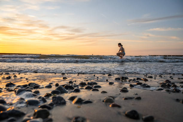 silhouette of little girl jumping over waves of baltic sea at sunset hour