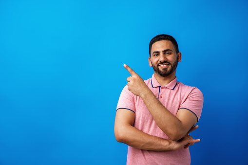 Young handsome arab man over beige background pointing to copy space and smiling, close up