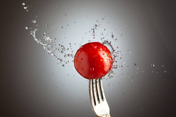 tomato cherry on a fork in splashes of water. Black white background