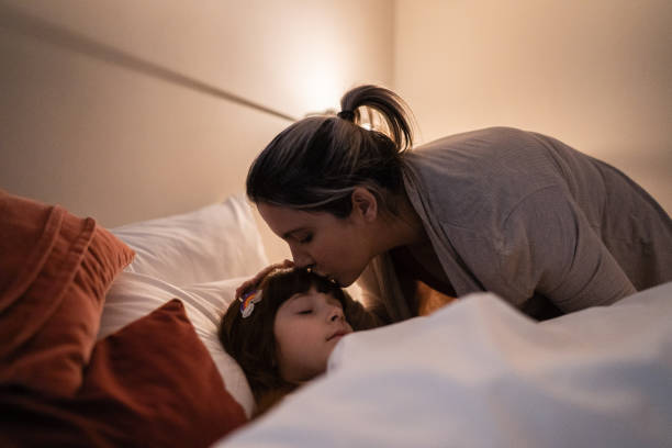 mutter setzt tochter zu hause schlafen - schlafenszeit stock-fotos und bilder