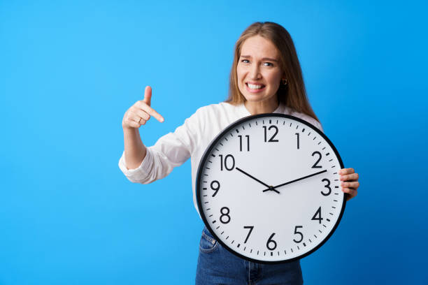 istock Attractive young woman holding big wall clock against blue background 1328361791