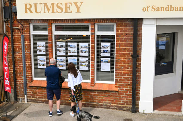 People looking in the window of an estate agency Poole, Dorset, England - June 2021: Two people looking at homes for sale in the window of an estate agent in Sandbanks near Poole Harbour. sandbanks poole harbour stock pictures, royalty-free photos & images