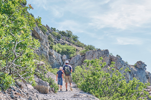 Boy and man hiking on scenic Golitsyn trail. Mountain landscape. National botanical reserve New World, Crimea. View from back. Local travel concept.
