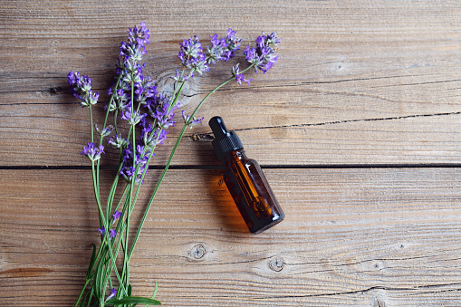 Aromatherapy: bunch of lavender flowers on wooden background and a brown bottle with essential oil, seen from above
