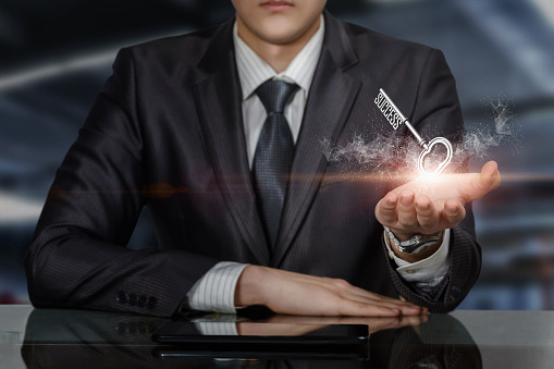 Businessman at the table shows the key to success on a blurred background.