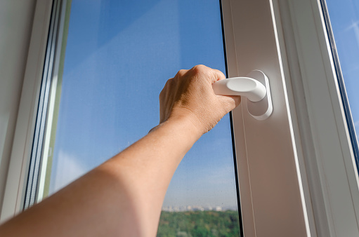 Woman's hand opens the handle of a plastic window against a blue sky