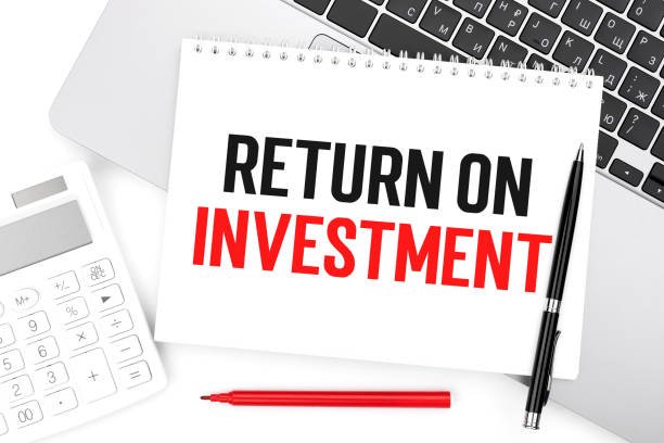 istock Text ROI - RETURN ON INVESTMENT on notebook, laptop, calculator, pen on white background. 1328378974