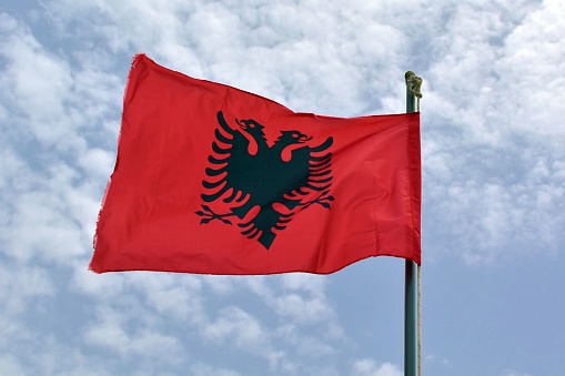 Albania national flag waving in wind on background of blue cloudy sky