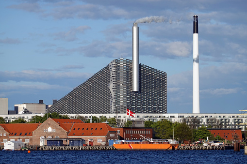 Tele shot of energy plant, Amager Bakke on a sunny afternoon in Copenhagen Denmark. Amager Bakke (Amager Hill) also known as Amager Slope or Copenhill, is a combined heat and power waste-to-energy plant and sports facility with skislope on the roof in Amager, Copenhagen, Denmark.