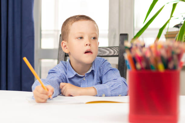 istock Cute seven year old child boy doing homework at home on a white wooden table during a pandemic. Selective focus. Close-up 1328380413