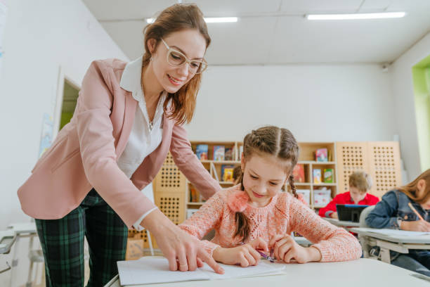 istock Female teacher helping schoolgirl pointing on something at her notebook 1328381683