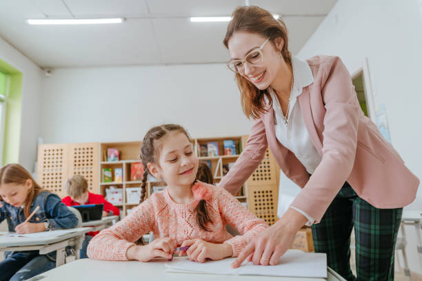 istock Female teacher helping schoolgirl pointing on something at her notebook 1328381695