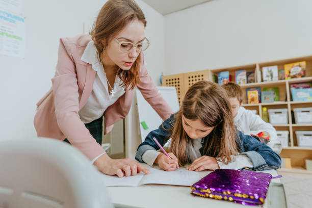 istock Female teacher helping schoolgirl pointing on something at her notebook 1328381704