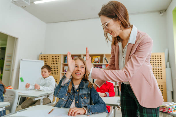 istock Female teacher helping schoolgirl pointing on something at her notebook 1328381725