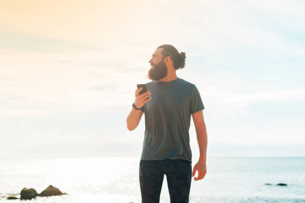istock Handsome bearded man holding mobile phone in his hand, texting message and looking away on tropical background. 1328382005