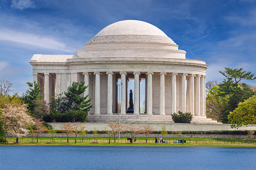 Jefferson Memorial with Silhouette of the Statue of Thomas Jefferson Seen Across the Tidal Basin with Blue Sky and Clouds, on a Beautiful Spring Morning, Washington DC, USA. Green Trees and Sightseeing Tourists are in the image. Canon EF 24-105mm/4L IS USM Lens.