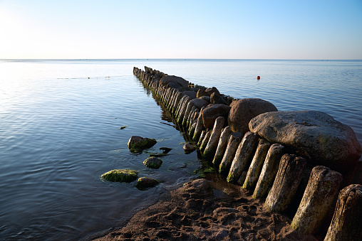 Old breakwater wooden pillars and stones at the Baltic Sea, blue sky and water