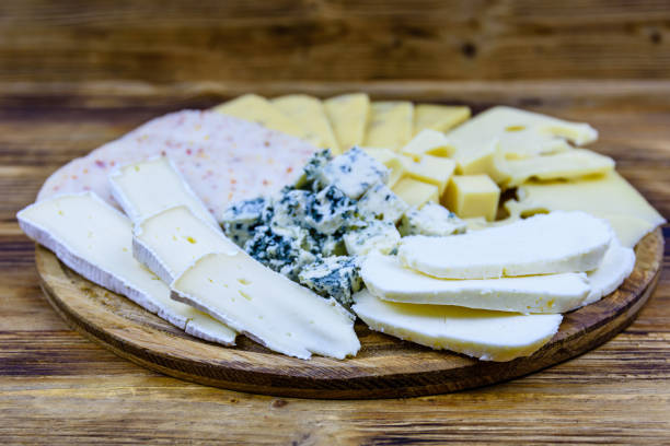 ломтики различных видов сыра на деревянном фоне. сырное блюдо - cheese tray cube swiss cheese стоковые фото и изображения