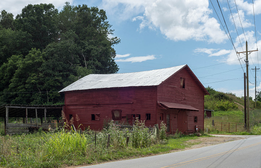 A red barn situated along a rural road with telephone poles to one side.
