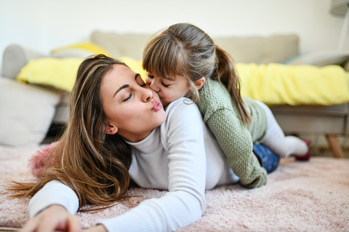 Mother And Daughter Kissing And Sharing Positive Emotions On Kitchen Floor