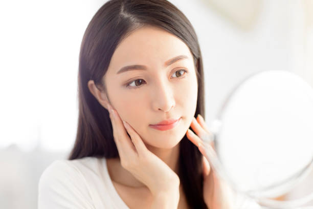 istock Young woman  touching face skin and looking in mirror 1328406515