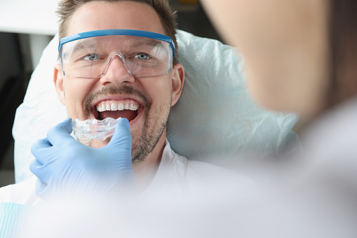 Doctor tries on plastic mouthguard for young smiling man to correct bite. Night mouth guards for bruxism concept
