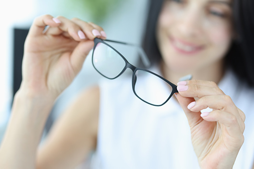 Young woman holds black glasses for vision in hands. Selection of fashionable frames concept