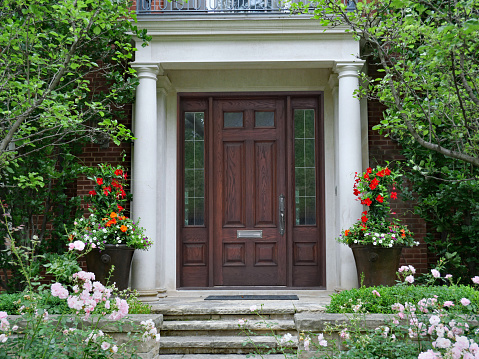 Ontario, Canada - July 12, 2021: Elegant wooden front door of house with columns and flower garden