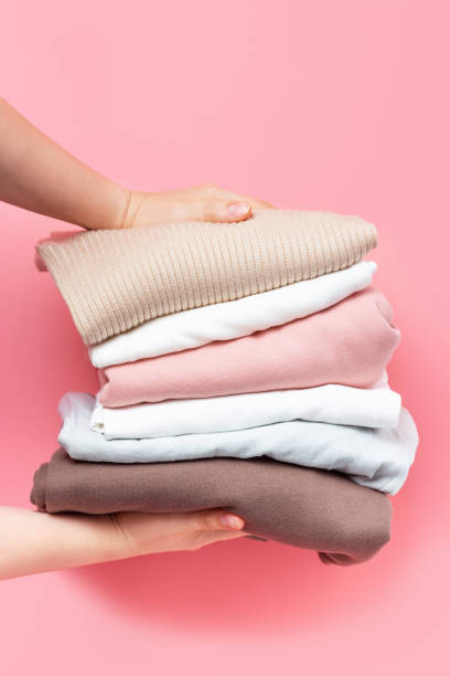 istock Female hands hold stack of knitted clothes on pink background close up. 1328417555