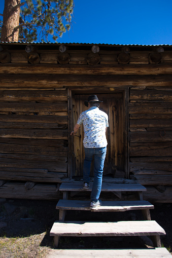 Man in Cowboy Hat and Jeans Entering Log Cabin