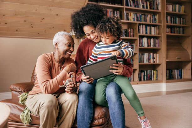 How Smart Home Tech Can Help Older Adults Three generation family sitting with tablet and laughing together distillery still photos stock pictures, royalty-free photos & images