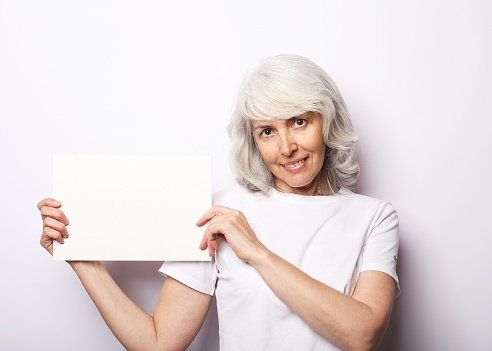 Portrait of happy senior woman wearing white t-shirt with blank advertising board or copy space