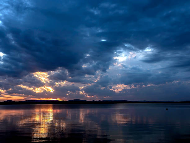 dark evening sky over the lake, dramatic clouds, the light of the sun is still visible, reflections on the water, summer evening, Southern Urals, Lake Uvildy