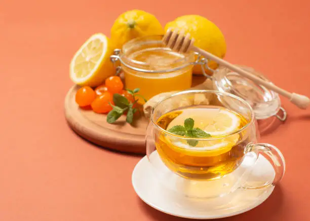 Ginger tea with mint and lemon. Healthy and hot drink. Liquid honey in honey-jar. Crystal cup on bright background. Selective focus. High quality photo