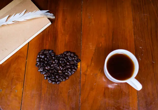 coffee cup on the table and black rose coffeebean. heart shape bean on wooden table. afternoon refreshing drink for coffee lover. hot black coffee in the white cup.