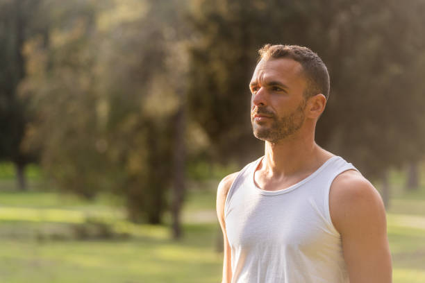 primer plano de un hombre adulto con el tanque superior blanco mirando hacia otro lado en el parque - tank top fotografías e imágenes de stock