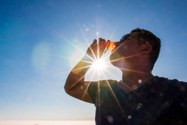 Man drinking from a small glass, sun rays and clouds.