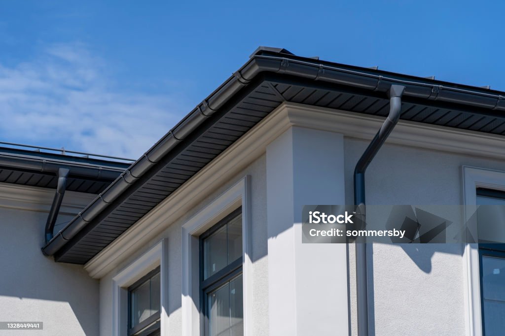 Corner of house with windows, new gray metal tile roof and rain gutter. Metallic Guttering System, Guttering and Drainage Pipe Exterior Roof Gutter Stock Photo