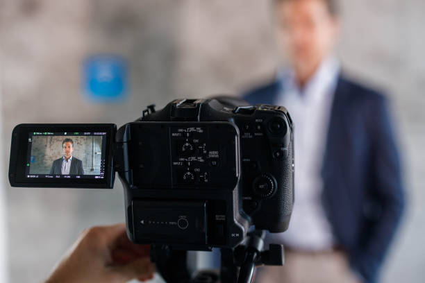 Close up of a camera filming male entrepreneur. Close up of a video camera filming mid adult businessman in the office. film studio stock pictures, royalty-free photos & images