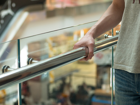 Man holding a hand rail in mall staircase closeup. Stock photo of the guy walking on the staircase. He's careful and doesn't want to fall