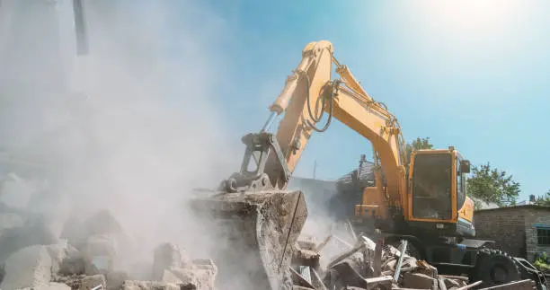 Photo of Destruction of old house by excavator. Bucket of excavator breaks concrete structure