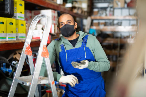 istock Warehouse worker in protective mask stands next to stepladder and tool shelves in hardware store 1328451585